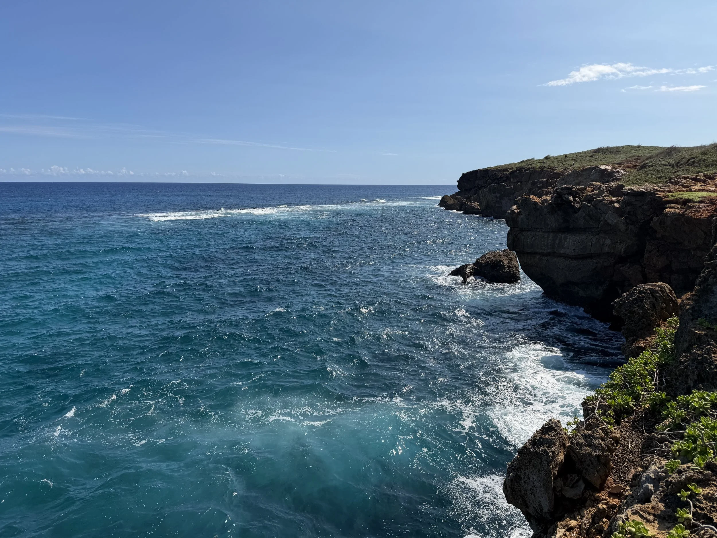 Ocean waves crashing against rocky cliffs under a clear blue sky on a sunny day.