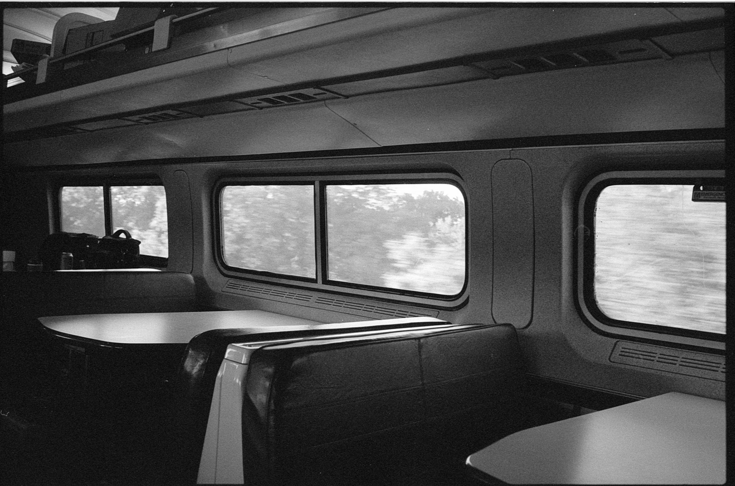 Inside of a train car, showing empty seats, side windows with blurred scenery outside, overhead luggage storage, and a table.