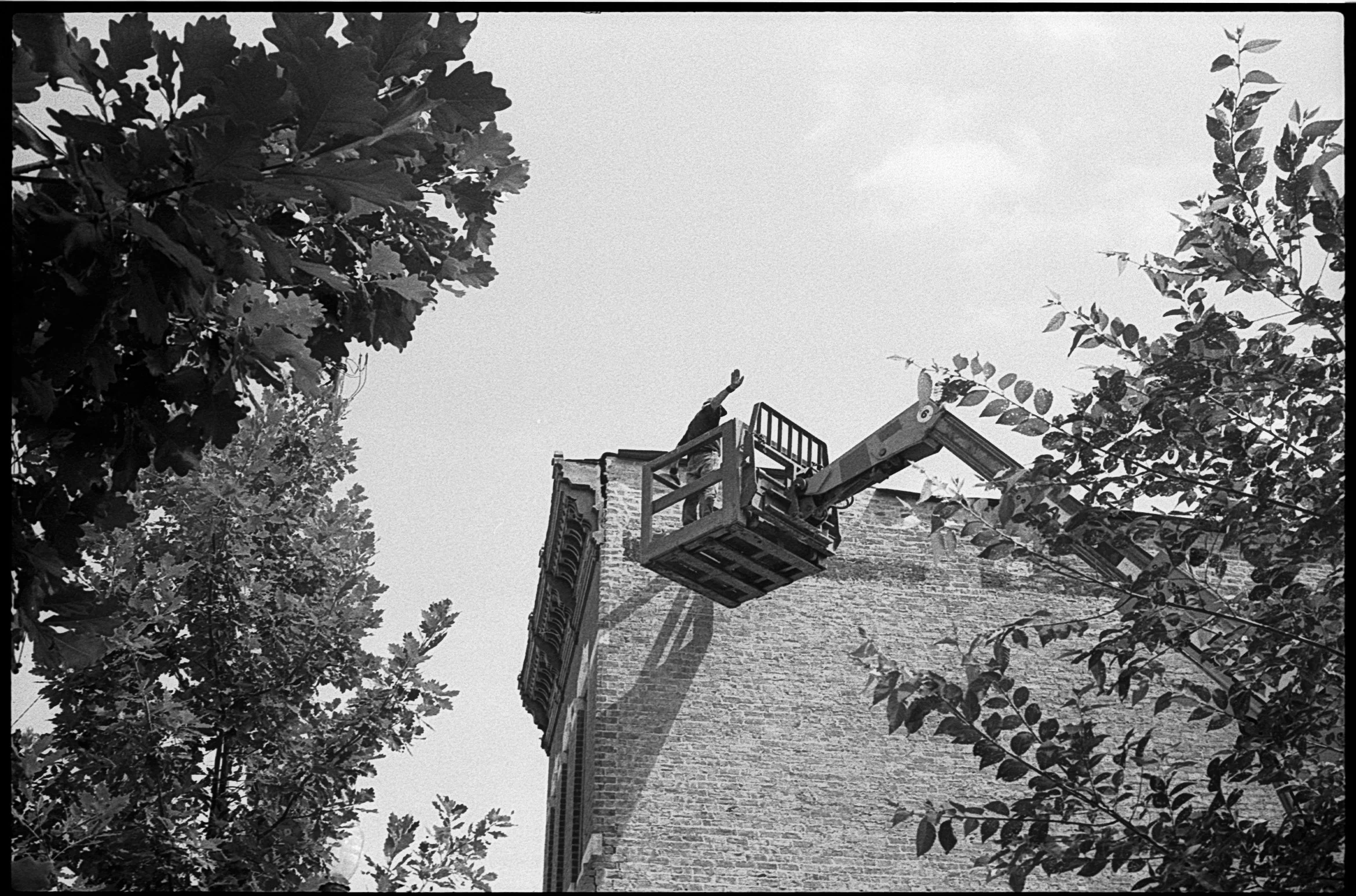 Person in a lift working on the top of a brick building tower, surrounded by trees and foliage.