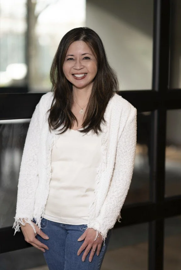 smiling dark haired female in a light silk shirt and ivory blazer and blue jeans