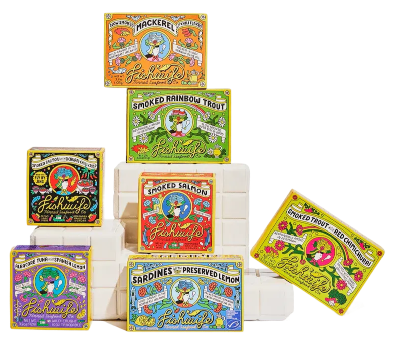 Arrangement of colorful seafood snack boxes including mackerel, smoked rainbow trout, smoked salmon, sardines with preserved lemon, and smoked trout with red chimichurri, displayed on white stacked blocks.