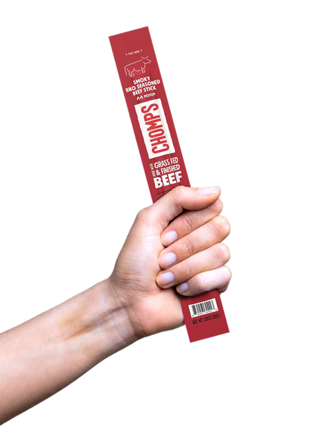 A hand holding a red package of Chomps smoky BBQ seasoned beef stick snack.