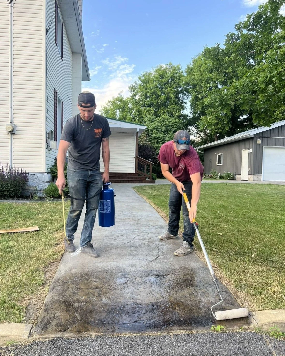 Two men cleaning a concrete sidewalk with a pressure washer and a roller.