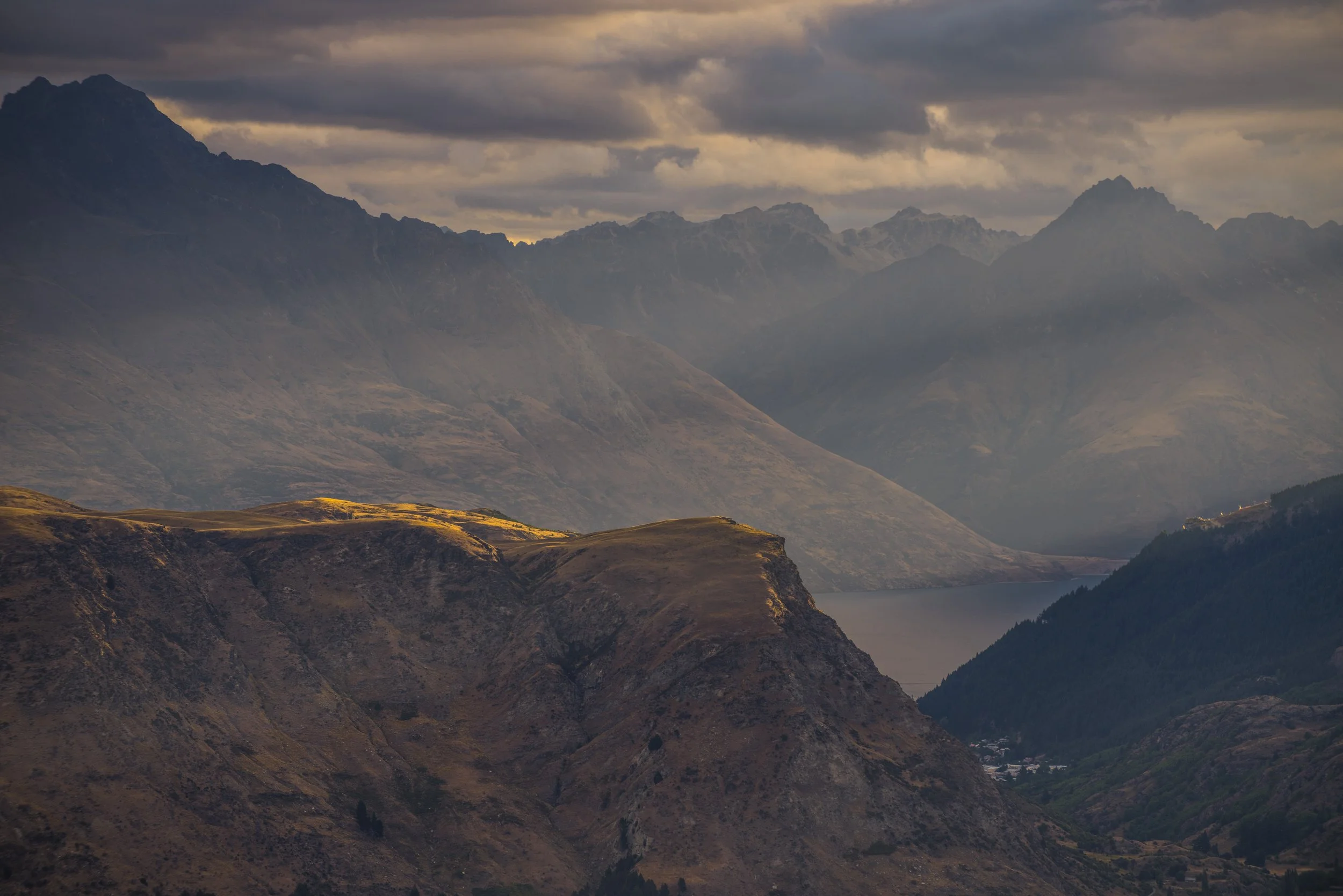 Mountain landscape with rugged peaks, valleys, a lake, and cloudy sky.