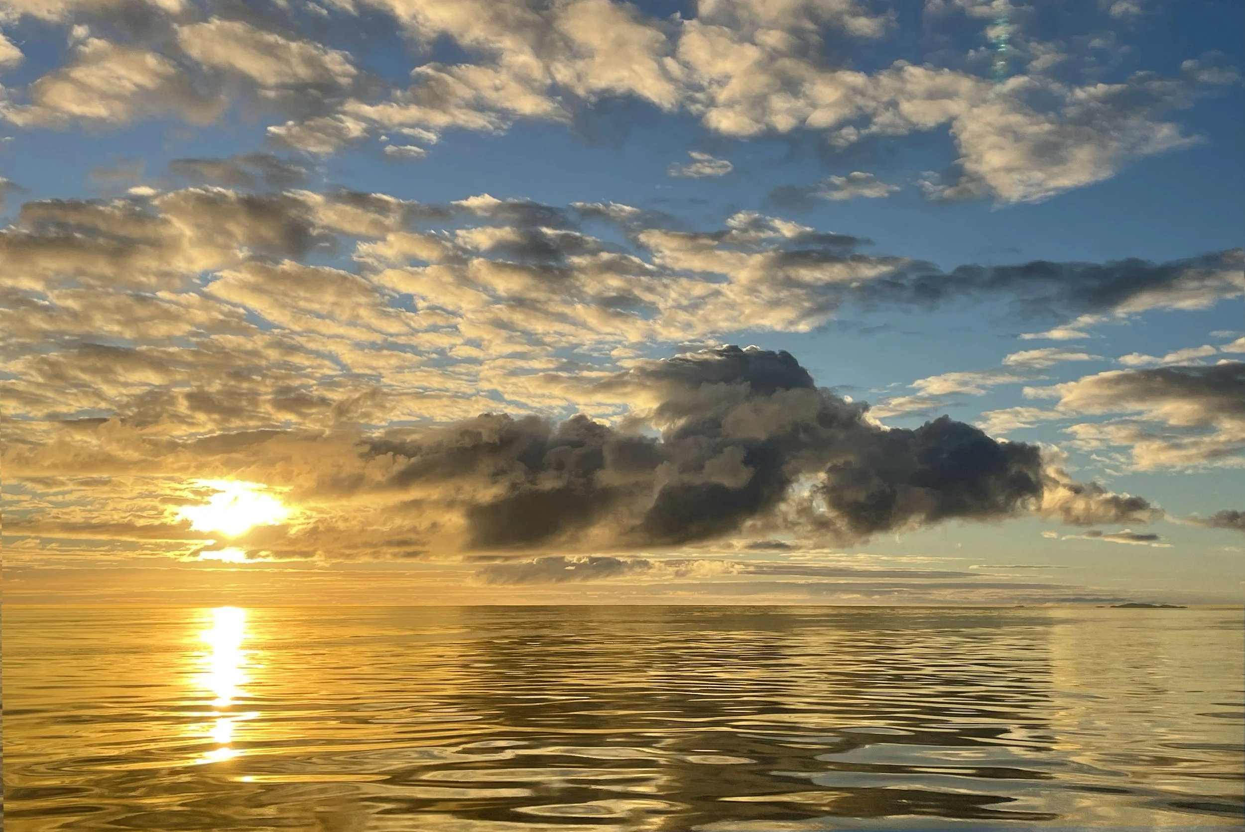 Sunset over calm ocean with partly cloudy sky, golden clouds reflecting on the water