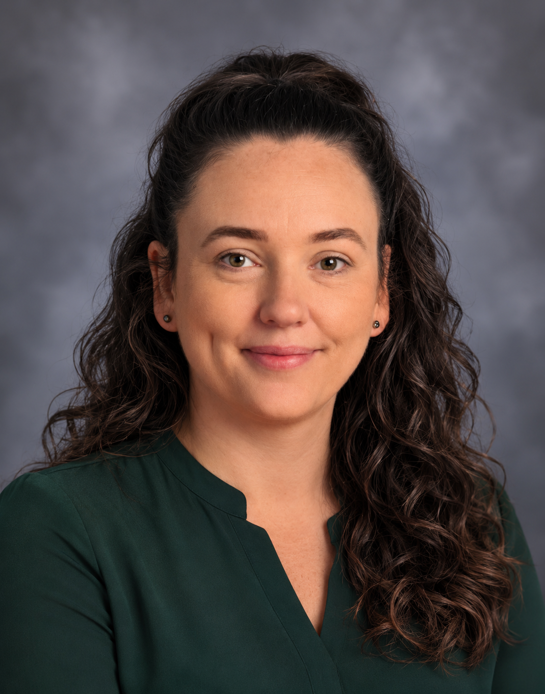 Amber Martinez, APRN. A woman with long dark hair and a dark green blouse, with a gray backdrop behind her.