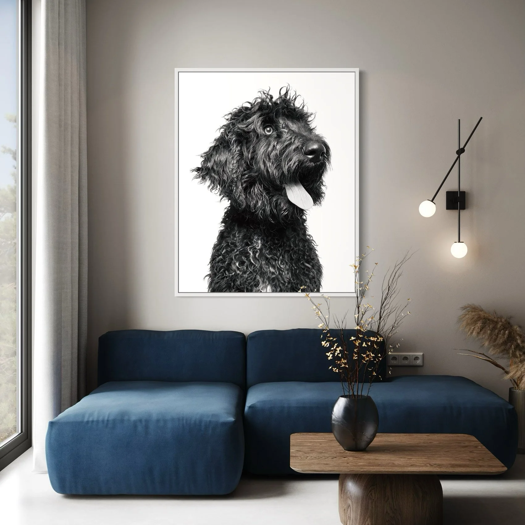 Living room with a large black and white portrait of a dog hanging on the wall above a dark blue sectional sofa. A wooden coffee table with a black vase holding branches is in front of the sofa. Modern wall lights and a large window are also visible.