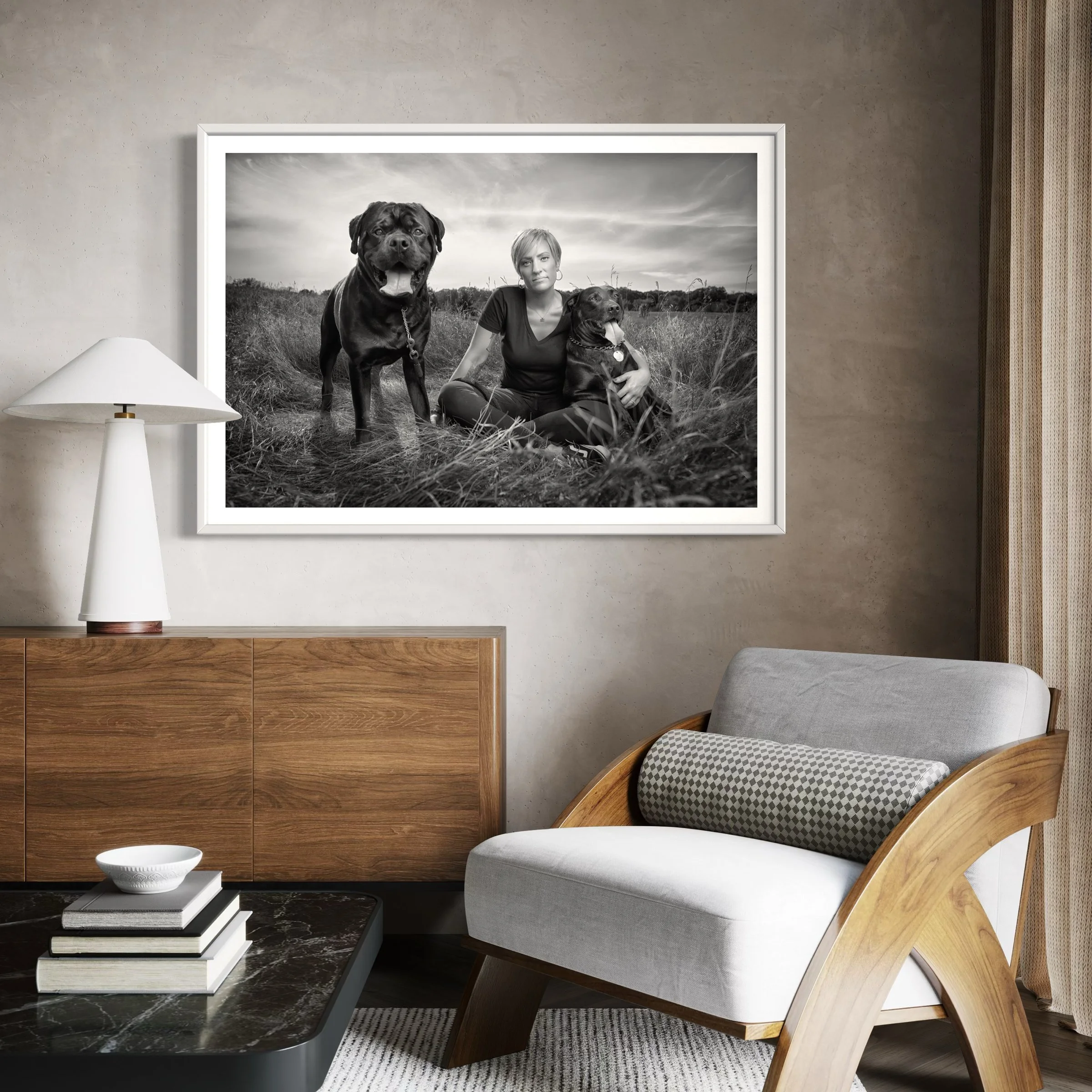 Black and white photograph of a woman sitting on grass with two large dogs, one standing and one sitting, outdoors with a cloudy sky in the background.