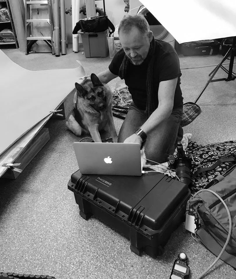 Tom and Quasimodo sitting on the floor of a photography studio, working on a laptop.