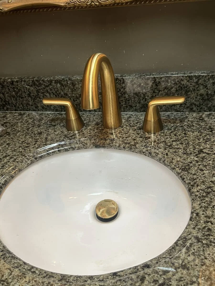 Bathroom sink with gold faucet and handles on granite countertop.