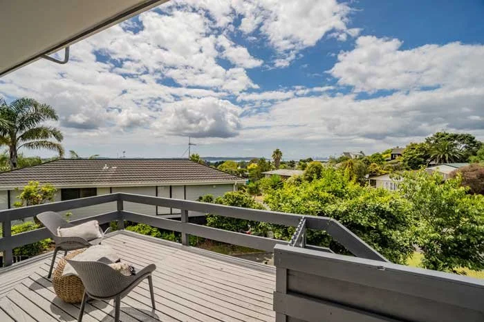 Sunny deck with chairs overlooking a residential area with trees and blue sky with clouds.