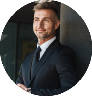 Professional man in a suit smiling with arms crossed, standing indoors against a dark wall.
