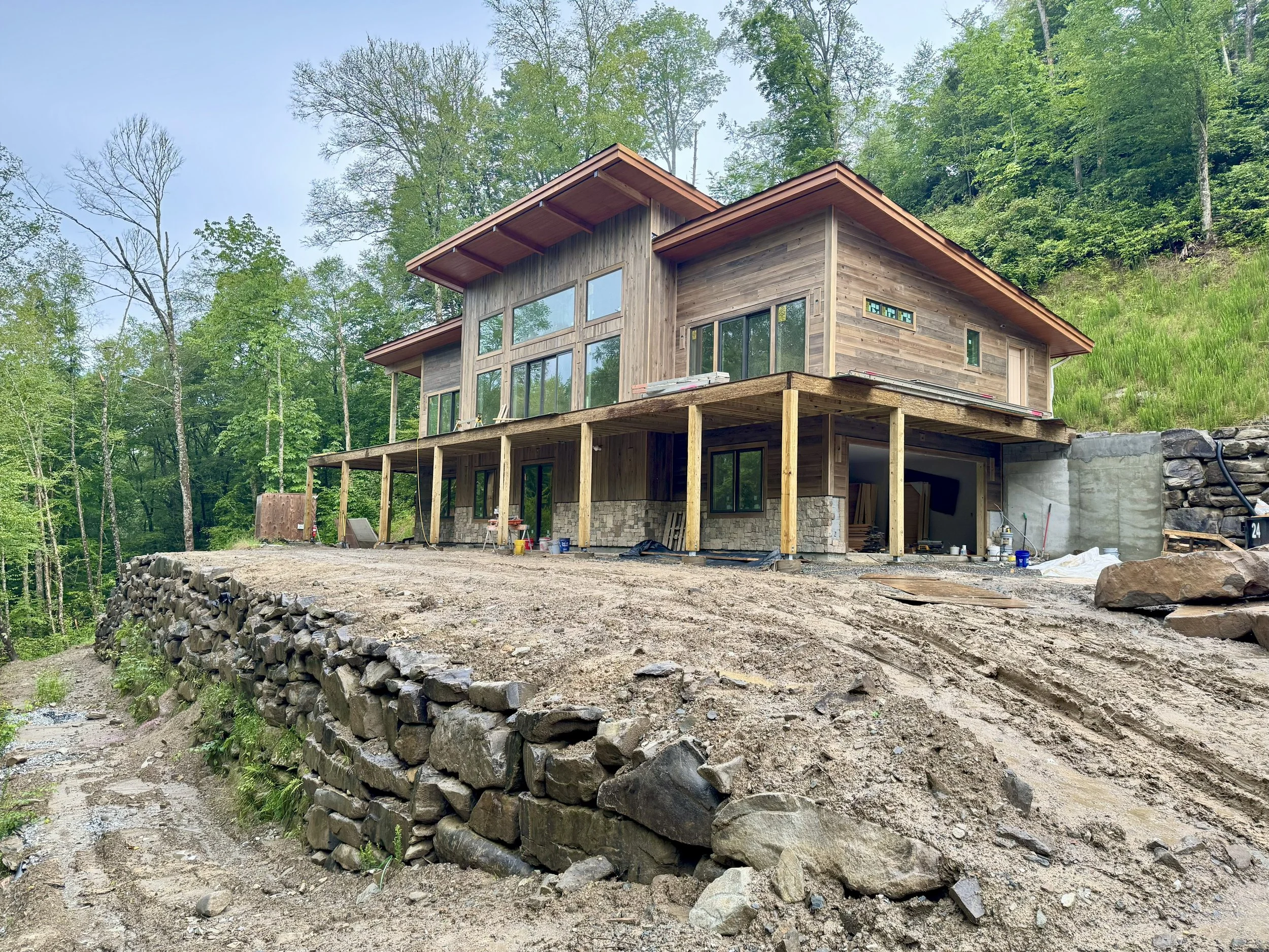 modern house under construction with dark cypress siding, soffit, large overhangs, exposed beams and columns, boulder retaining walls