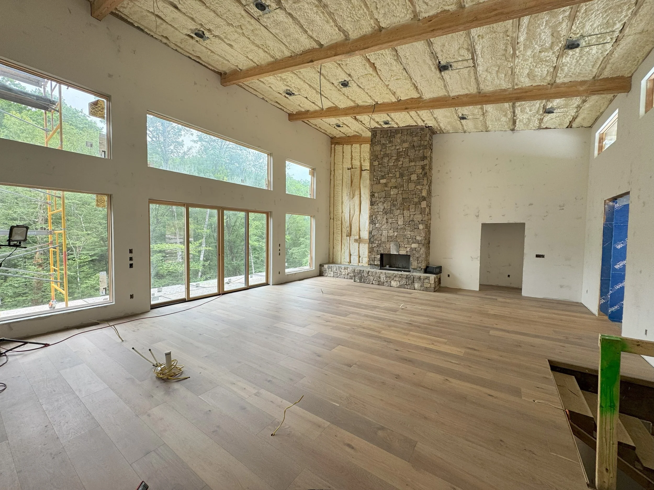 house under construction showing a newly installed white oak hardwood floor, open floor plan ceiling beams, open floor plan, and floor to ceiling stone fireplace