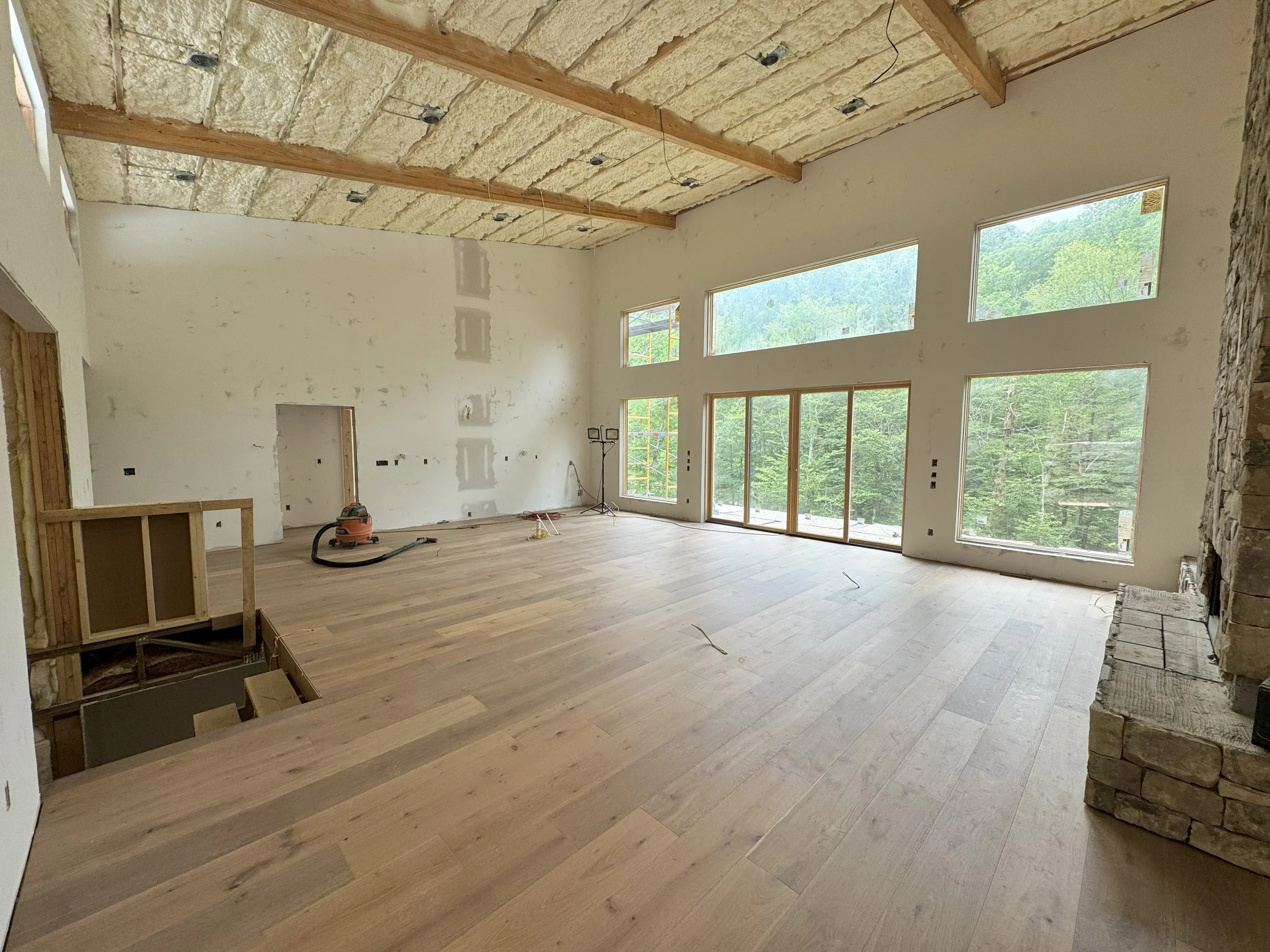 house under construction showing a newly installed white oak hardwood floor, open floor plan ceiling beams, open floor plan