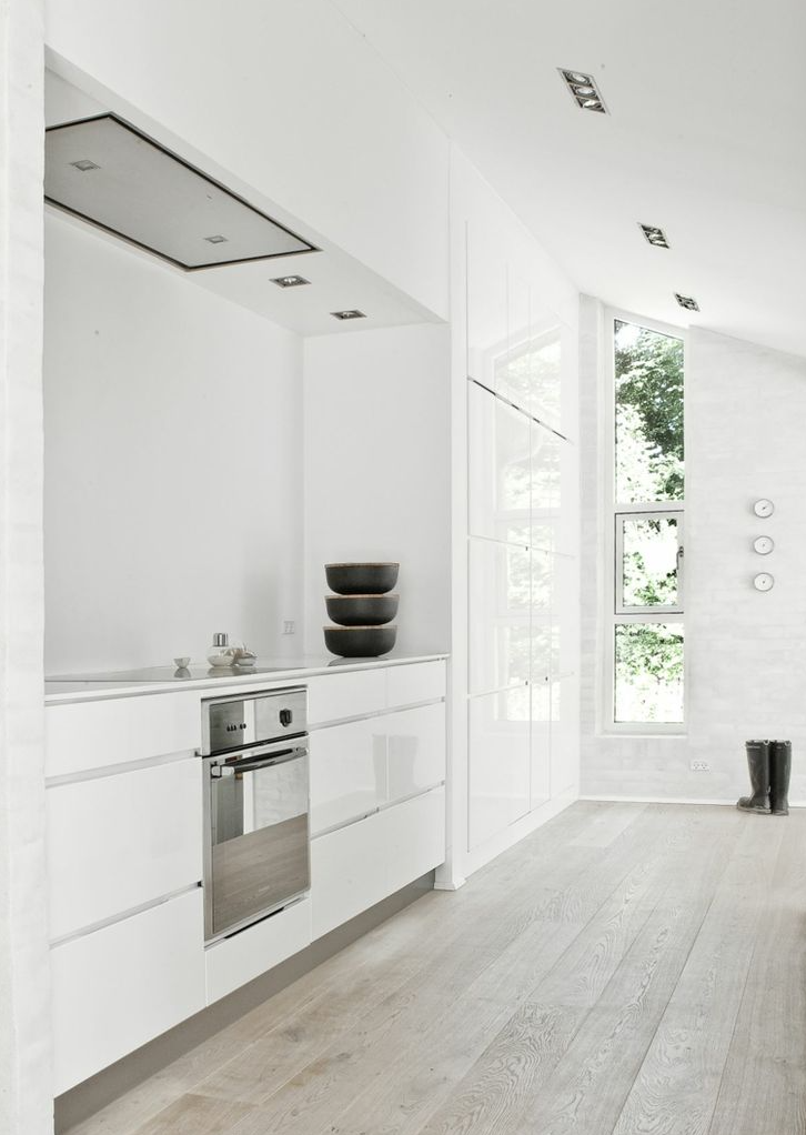 Cocina moderna con gabinetes blancos, horno empotrado, tres tazones negros apilados en la esquina, ventanas grandes que dejan entrar luz natural y botas negras al lado.