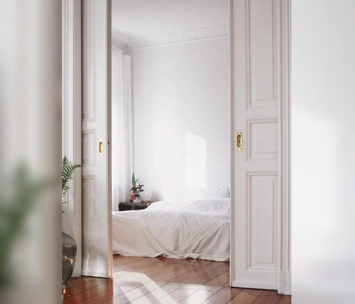 Dormitorio con paredes blancas y cama con sábanas blancas, vista a través de puertas corredizas blancas.