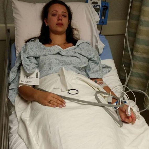 Young woman lying in a hospital bed, appearing to be recovering after an illness or medical procedure, with medical equipment attached.