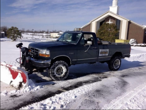 Pickup truck with snow plow attachment clearing snowy church driveway
