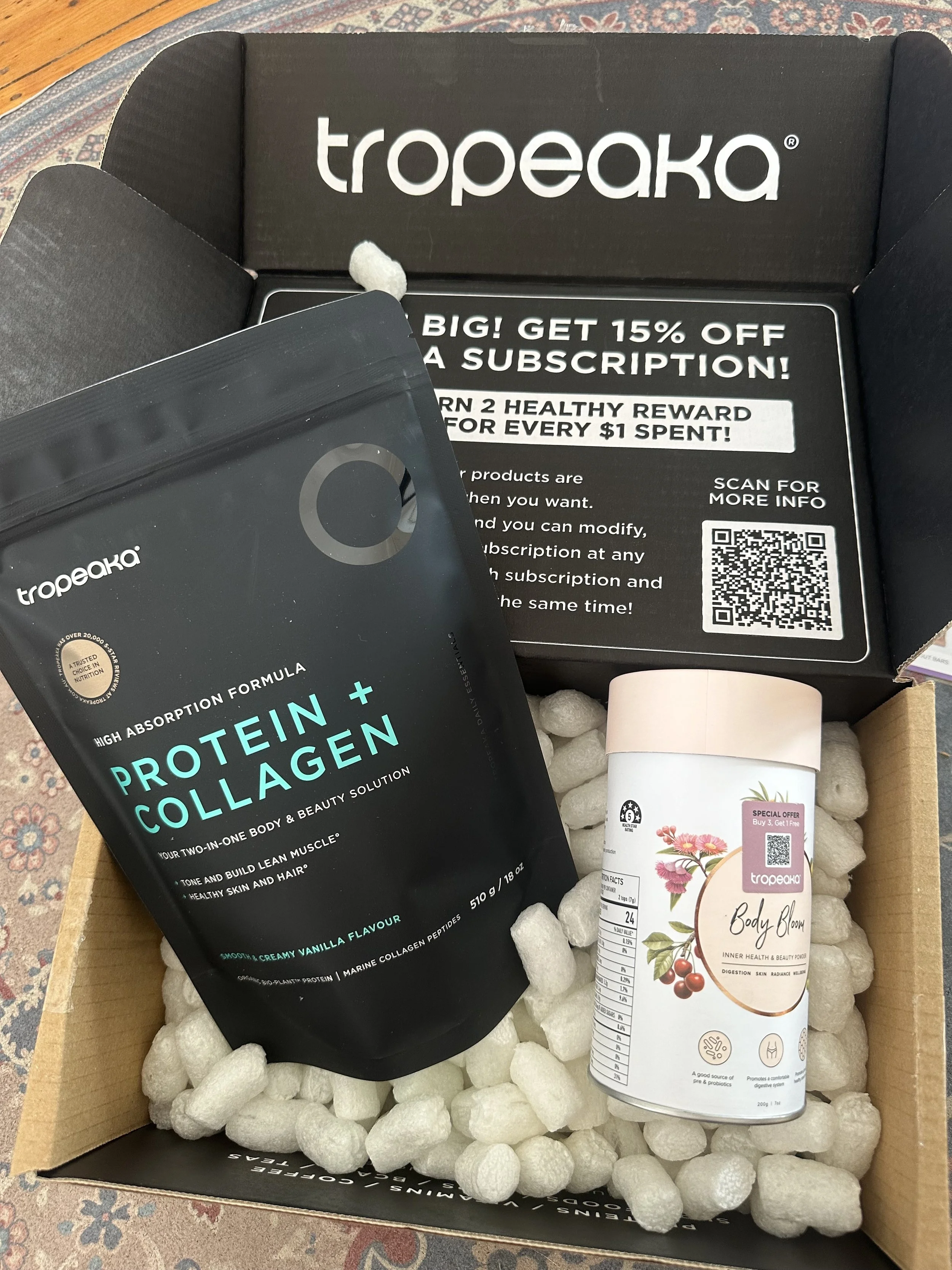 Open box containing Tropeaka protein powder package, a Tropeaka Body Bloom container. Brand Partnership