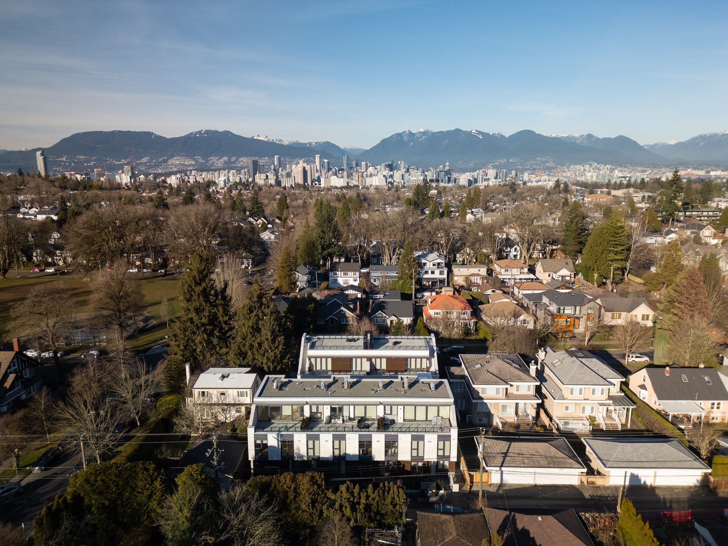 Aerial view of a residential neighborhood with houses, trees, and distant city skyline against mountains.