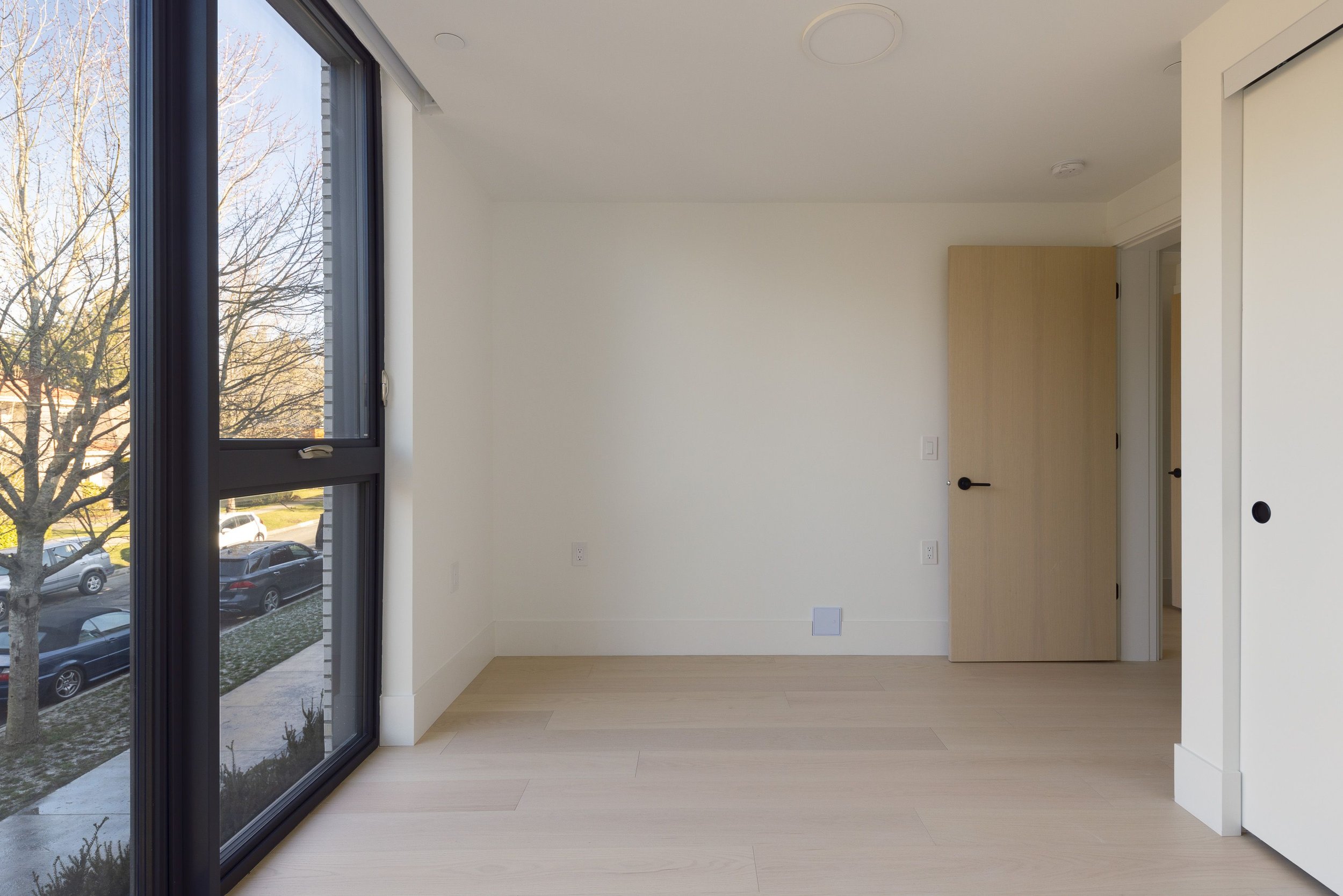 Empty room with large window, wooden floor, and open door
