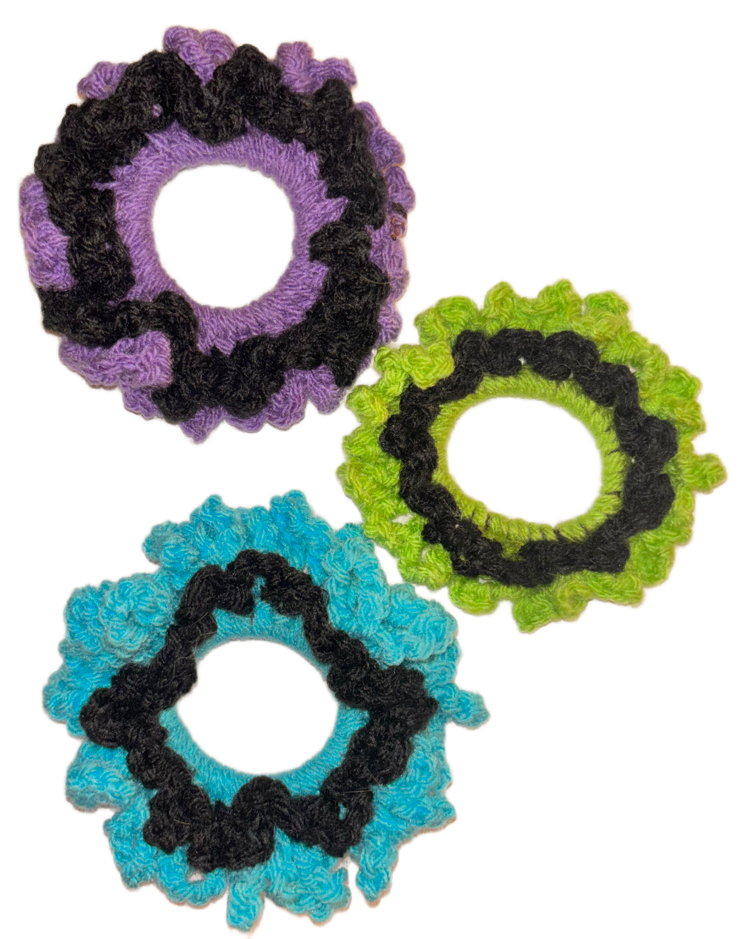 Colorful crocheted hair ties in purple, green, and blue with black decorative elements.