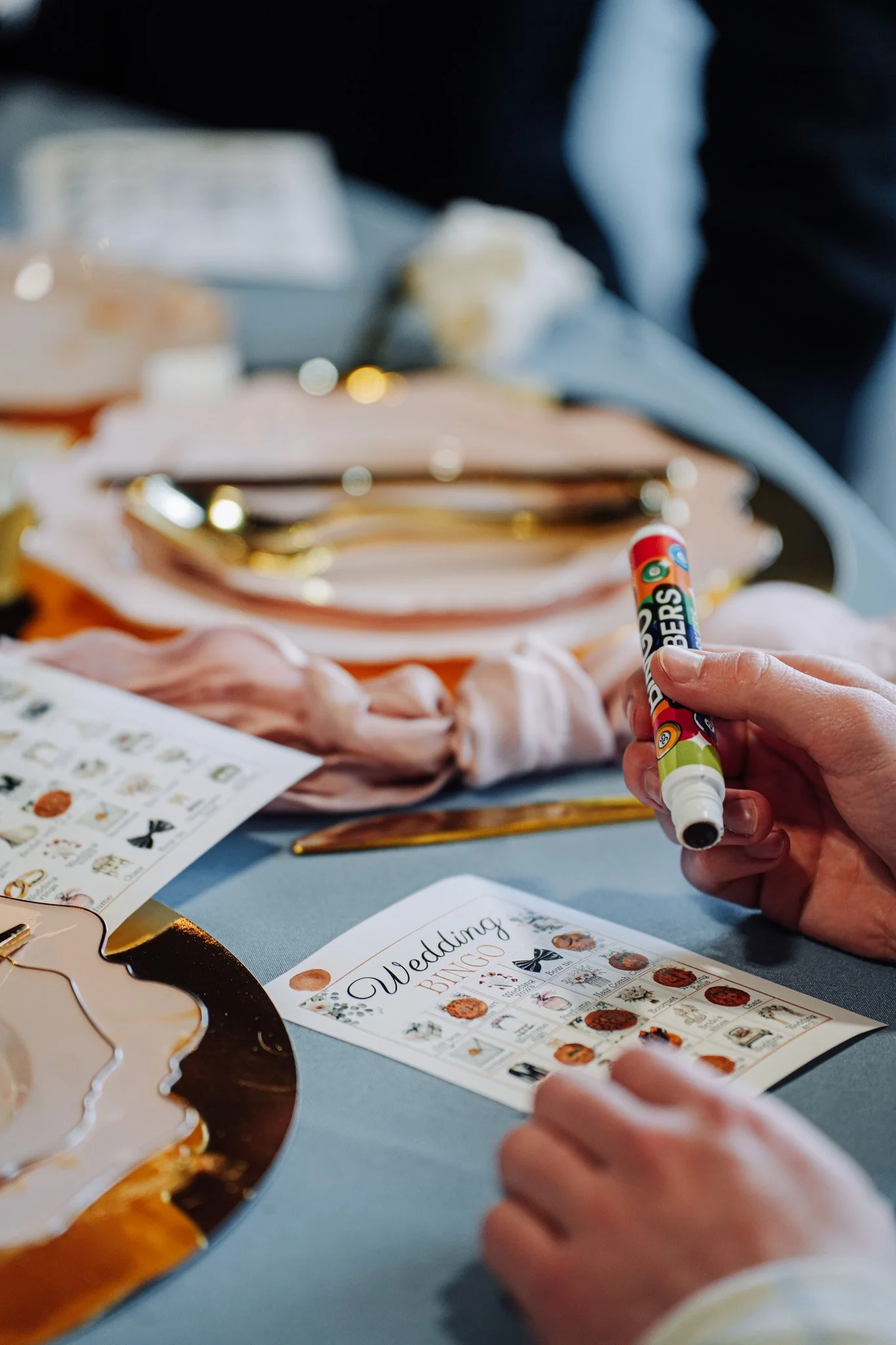 Person writing on a wedding bingo card with a red and green marker at a decorated table.