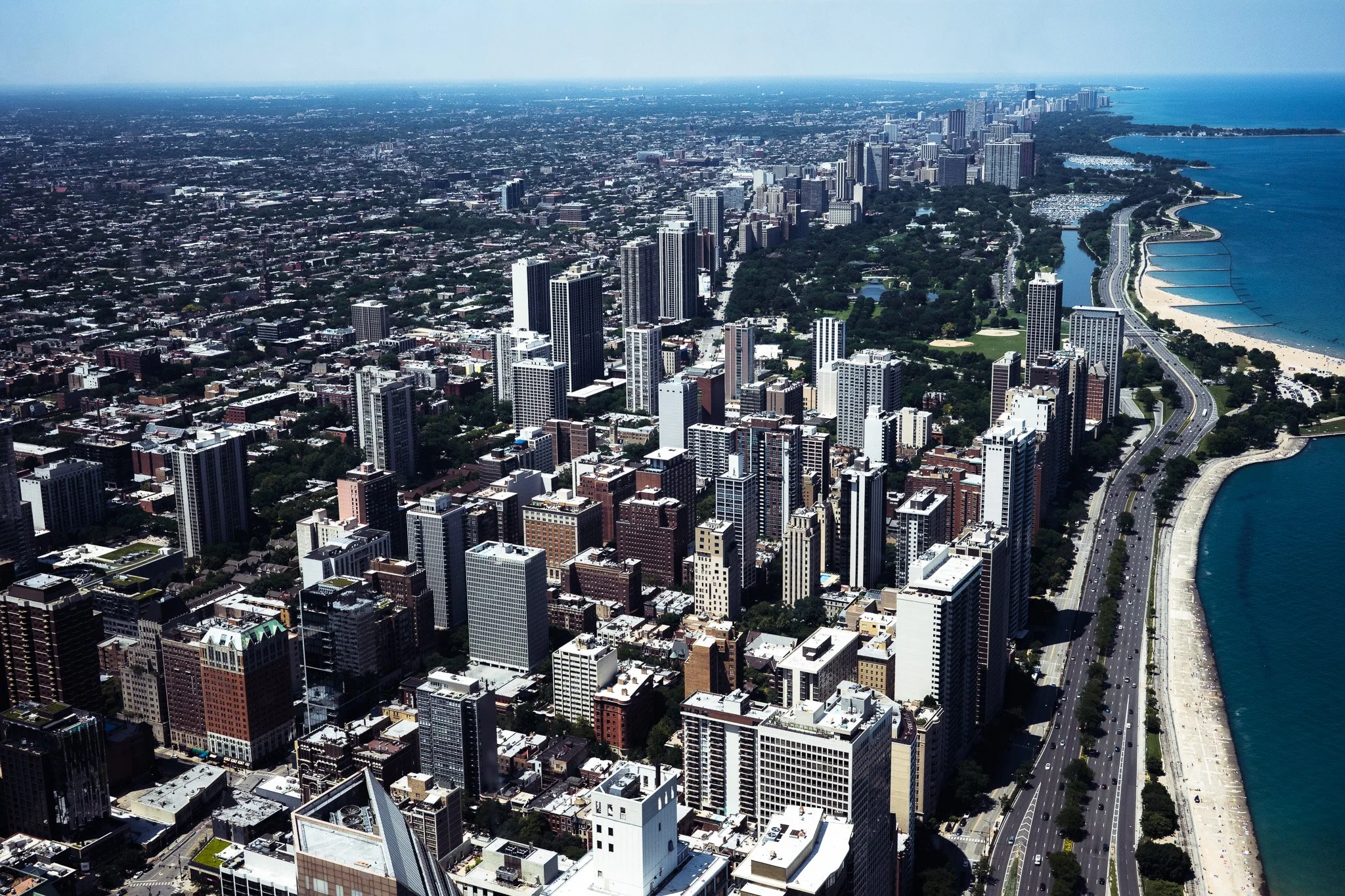 Aerial view of Chicago’s downtown skyline along Lake Michigan, with Lake Shore Drive, beaches, parks, and high-rise buildings.