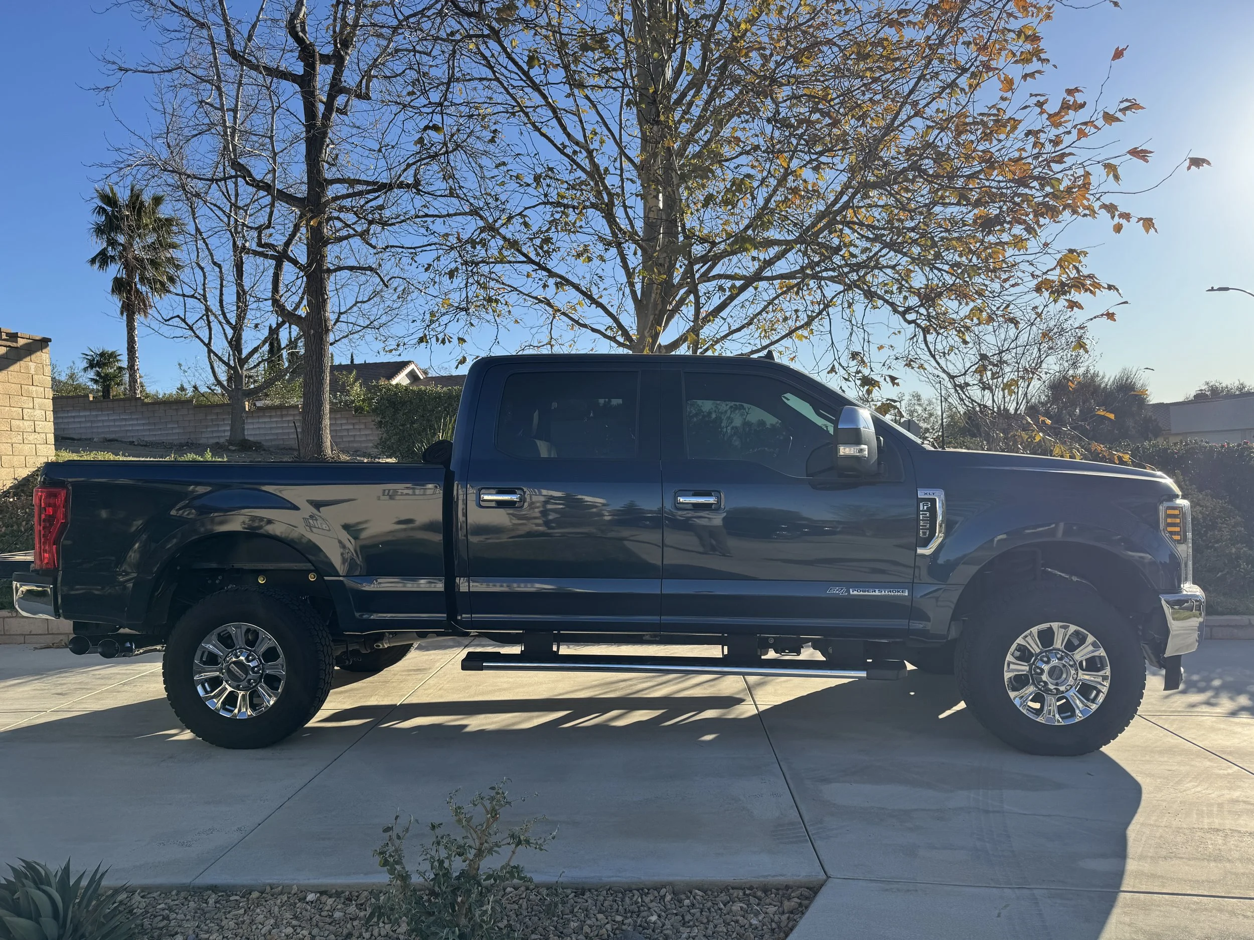 A black pickup truck parked on a driveway with trees and a clear blue sky in the background.