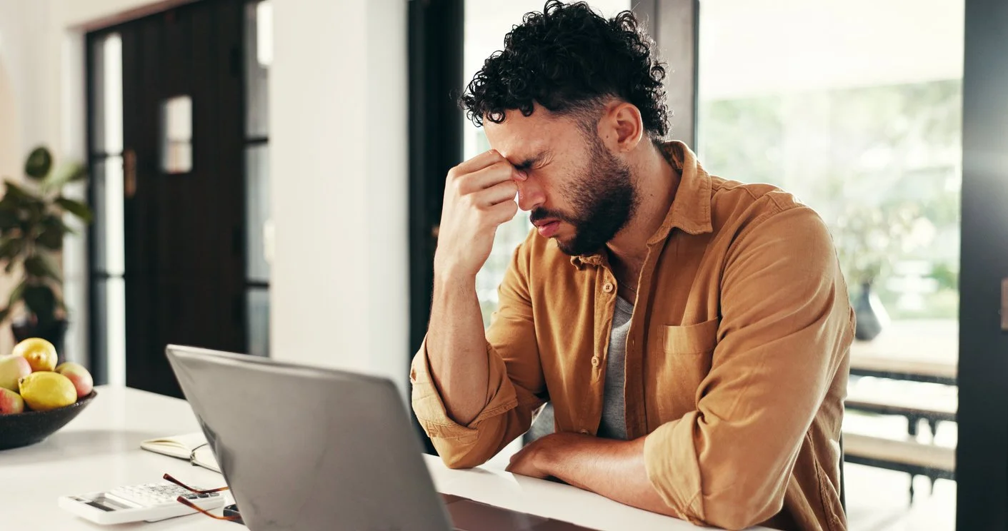 a man at his desk working on a laptop and struggling with brain fog and mental fatigue