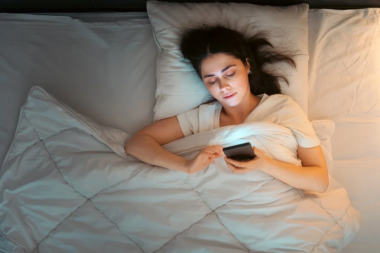woman having trouble sleeping and using smartphone lying in bed at night.
