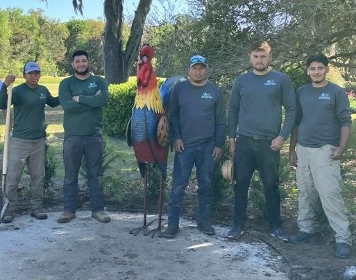 Five men standing outdoors with a large colorful turkey statue in the center, trees and a grassy area in the background.