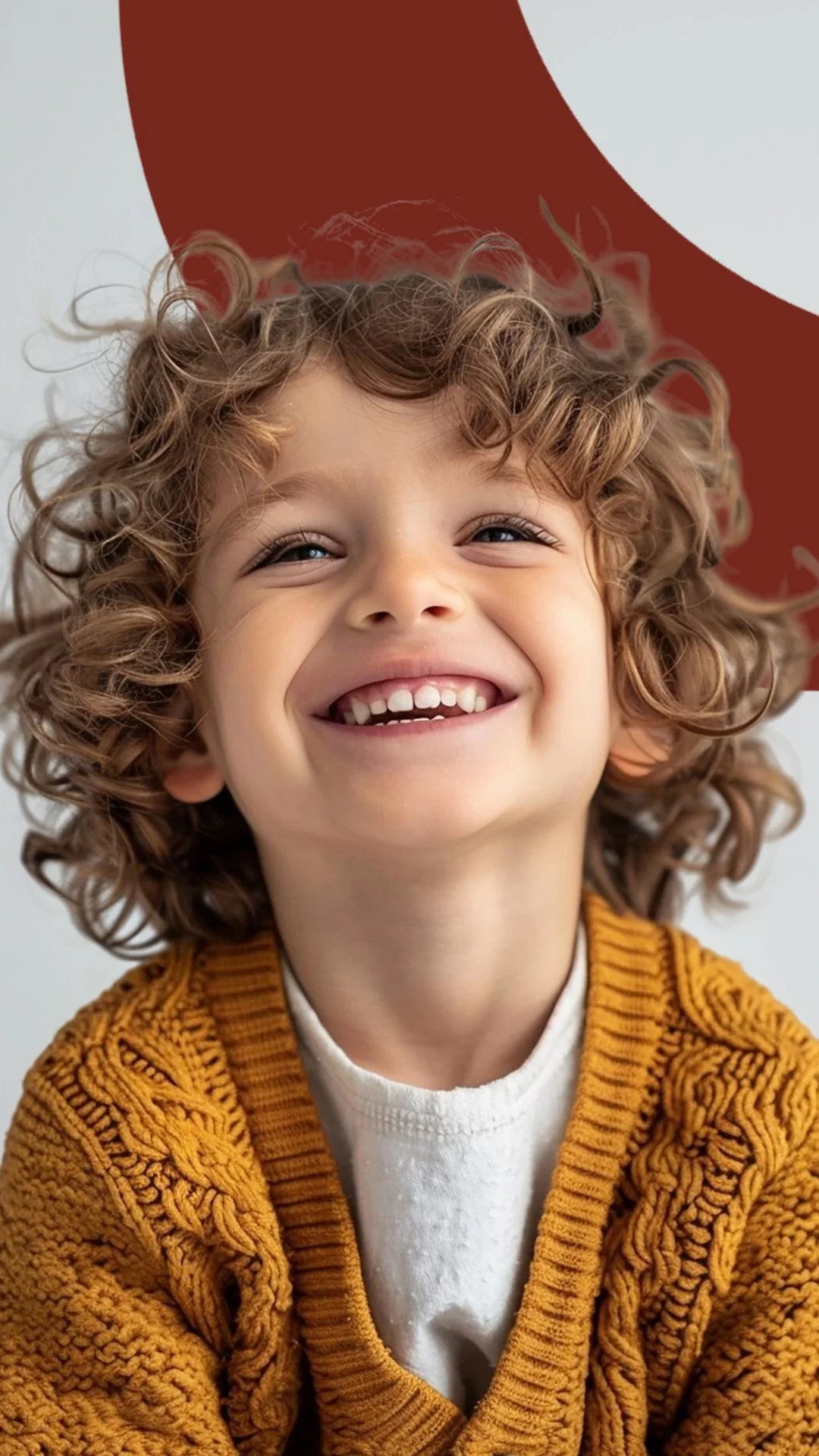 Smiling child with curly hair wearing a mustard-colored sweater.