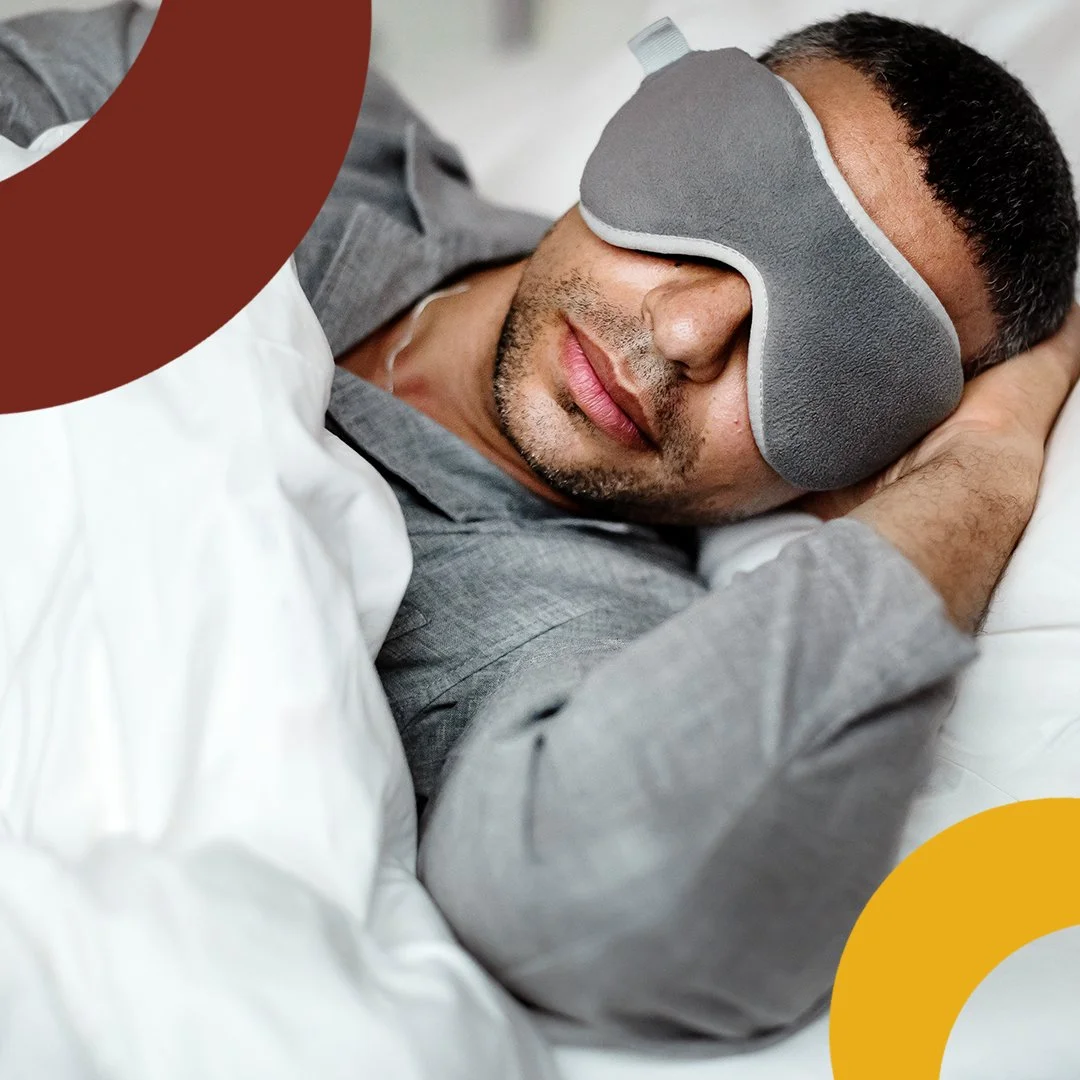 Man sleeping with eye mask, wearing gray pajamas, in bed with white sheets.