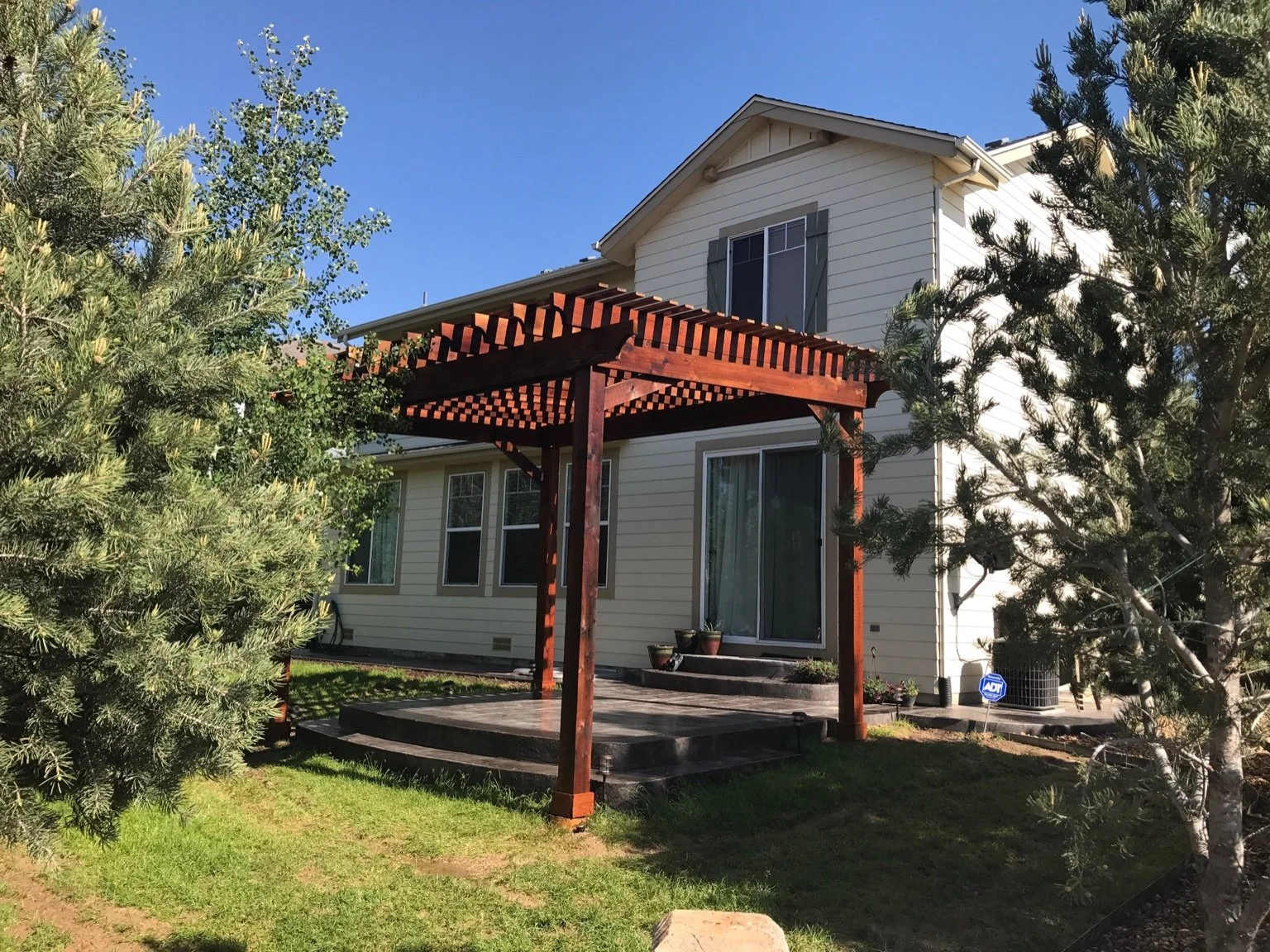 Backyard with a well-maintained green lawn, a curved white gravel path, a brown wooden fence, and neighboring houses in the background under a clear blue sky.