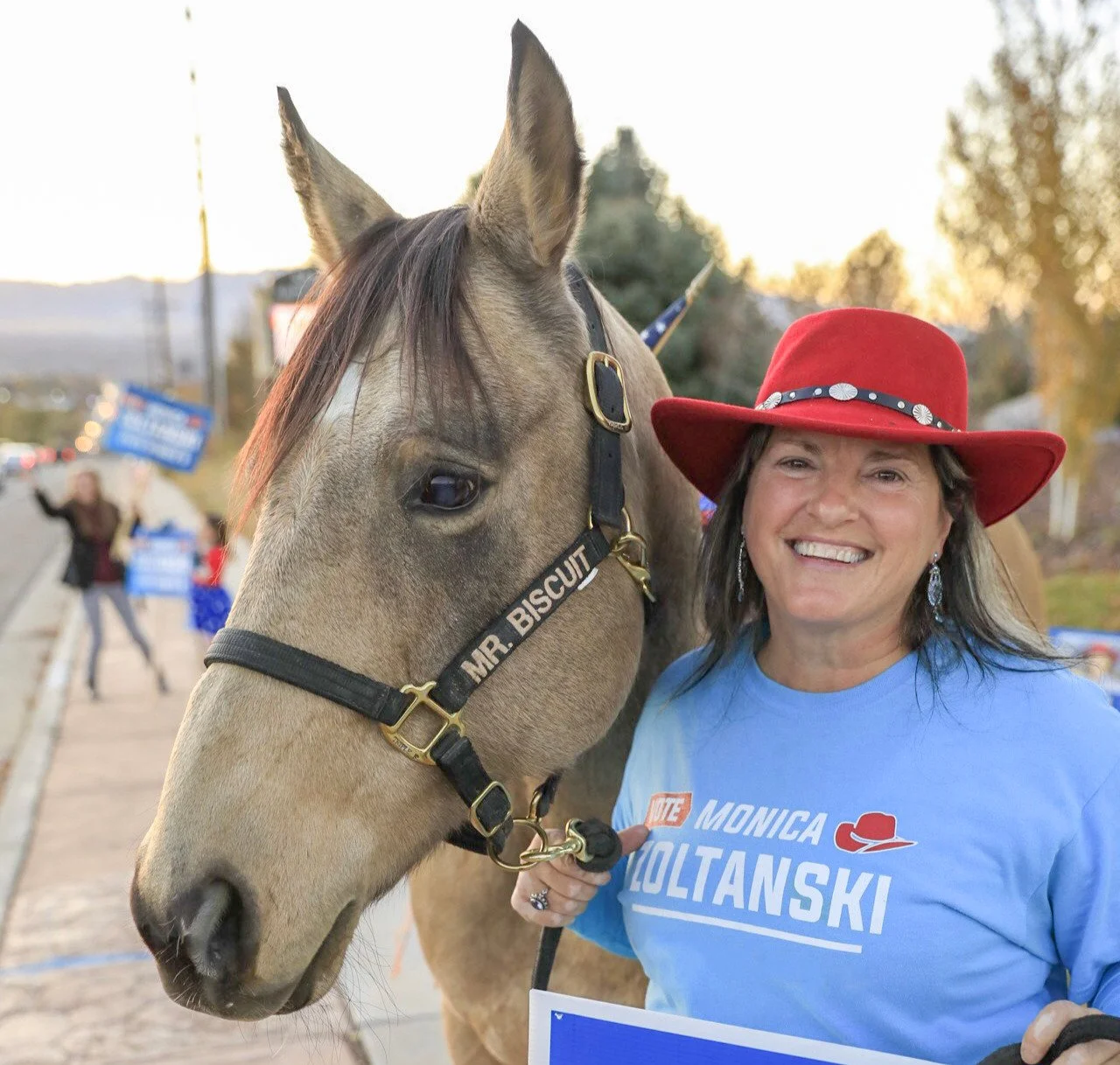 Monica Z smiles alongside her horse, Mr. Biscuit, embodying her down-to-earth leadership and love for the community. Together, they represent a strong bond with both nature and the values of dedication.