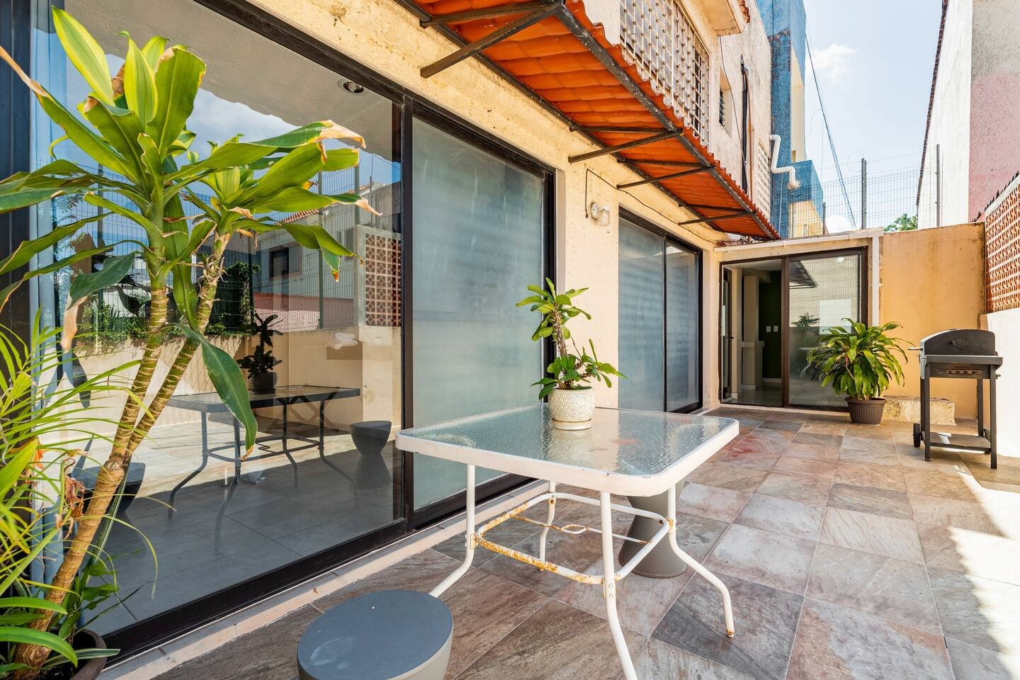 Outdoor patio with glass table, potted plants, grill, and large sliding glass doors.