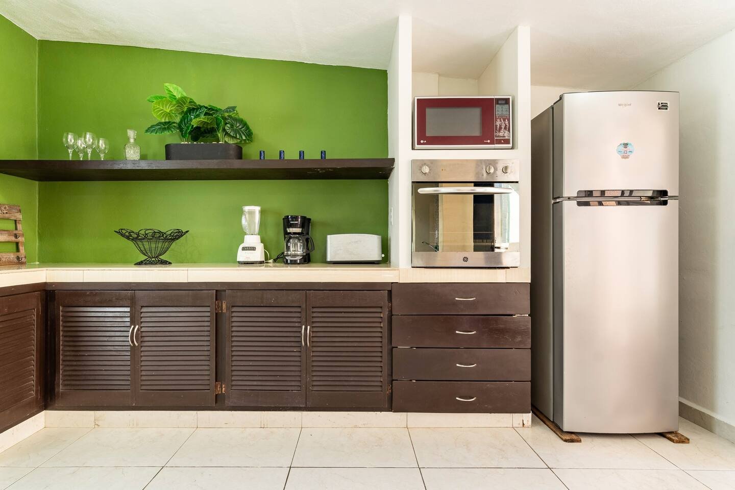 Modern kitchen with green walls, dark wood cabinets, stainless steel refrigerator, oven, microwave; small appliances like a blender and coffee maker on the counter.