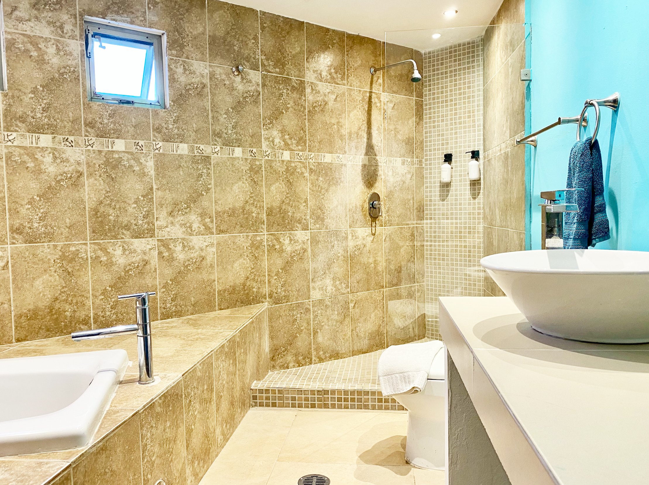 Modern bathroom with beige tile walls, a glass shower enclosure, white basin sink, chrome faucet, and blue accent wall.