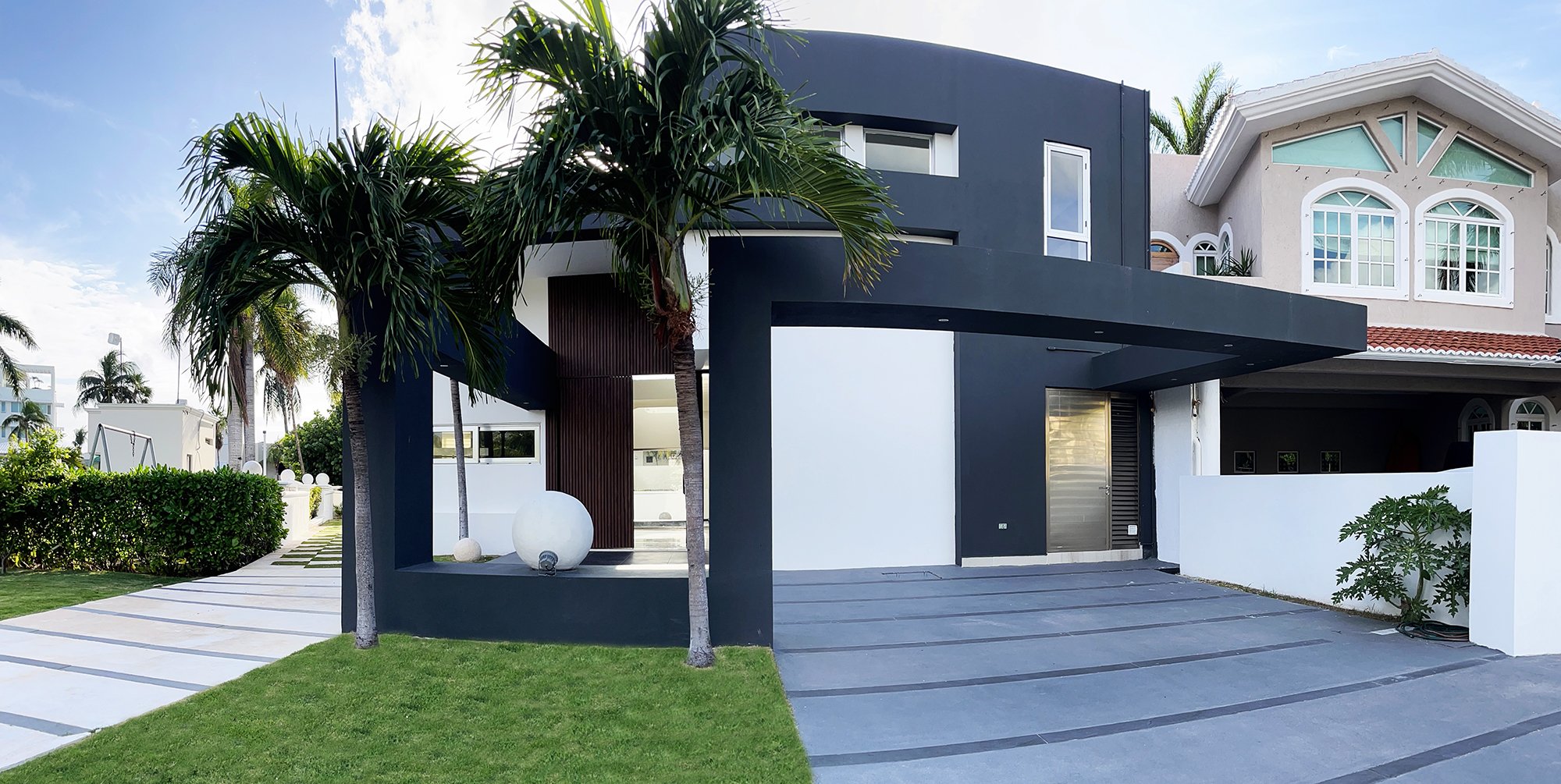 Modern house with dark and light exterior, palm trees, and large windows.