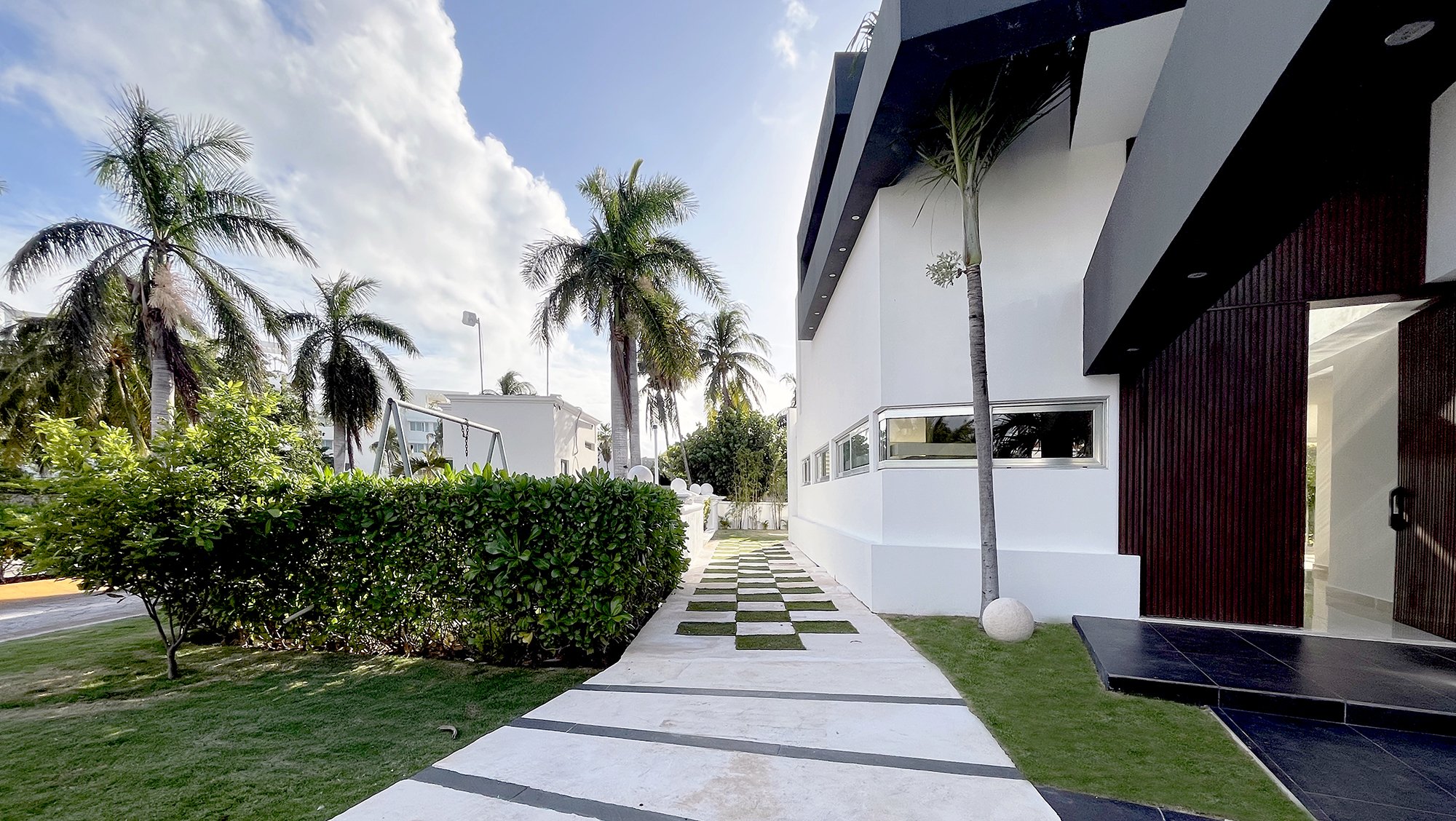 Modern building exterior with palm trees and a paved path in a landscaped garden.