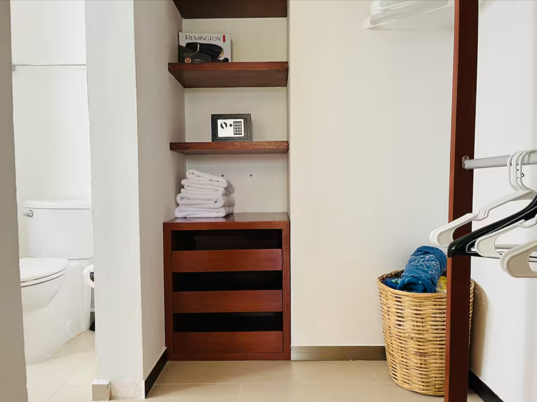 Bathroom with wooden shelves, a small safe, stack of white towels, wicker basket with towels, and clothes hangers.