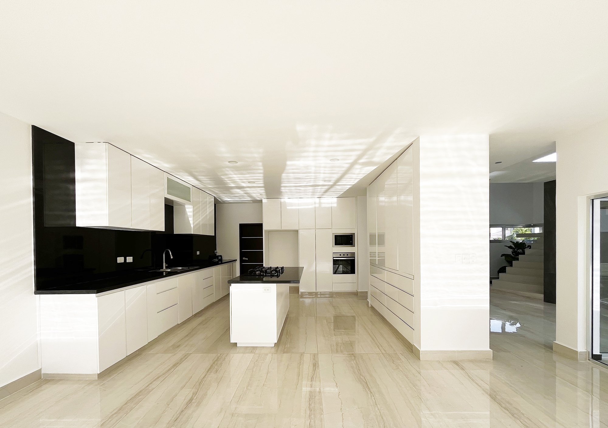 Modern kitchen with white cabinetry, black countertops, an island with stove, built-in oven, and microwave.
