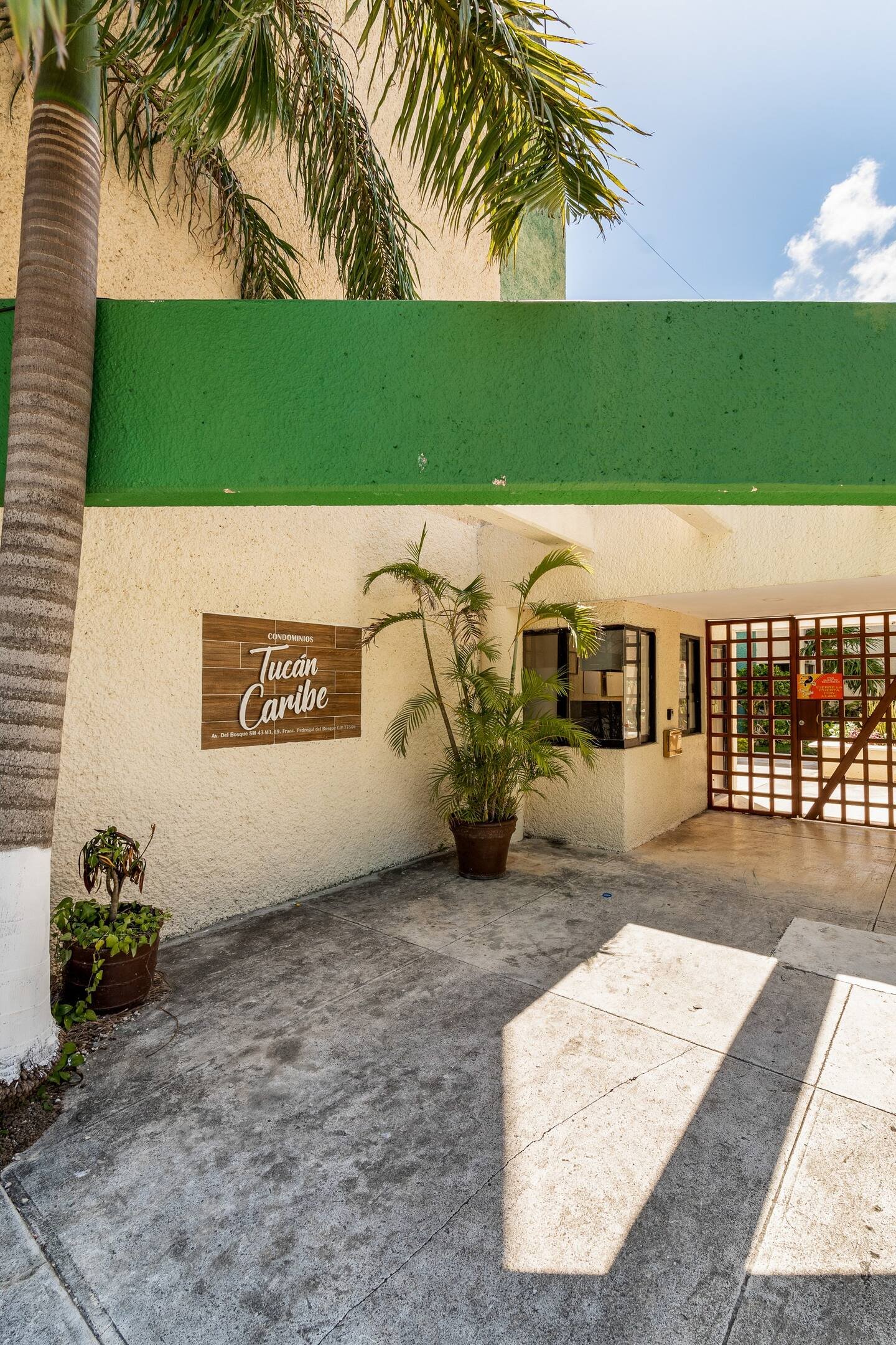 Entrance of a building with a sign reading 'Tucán Caribe' on the wall, featuring potted plants and a green awning.