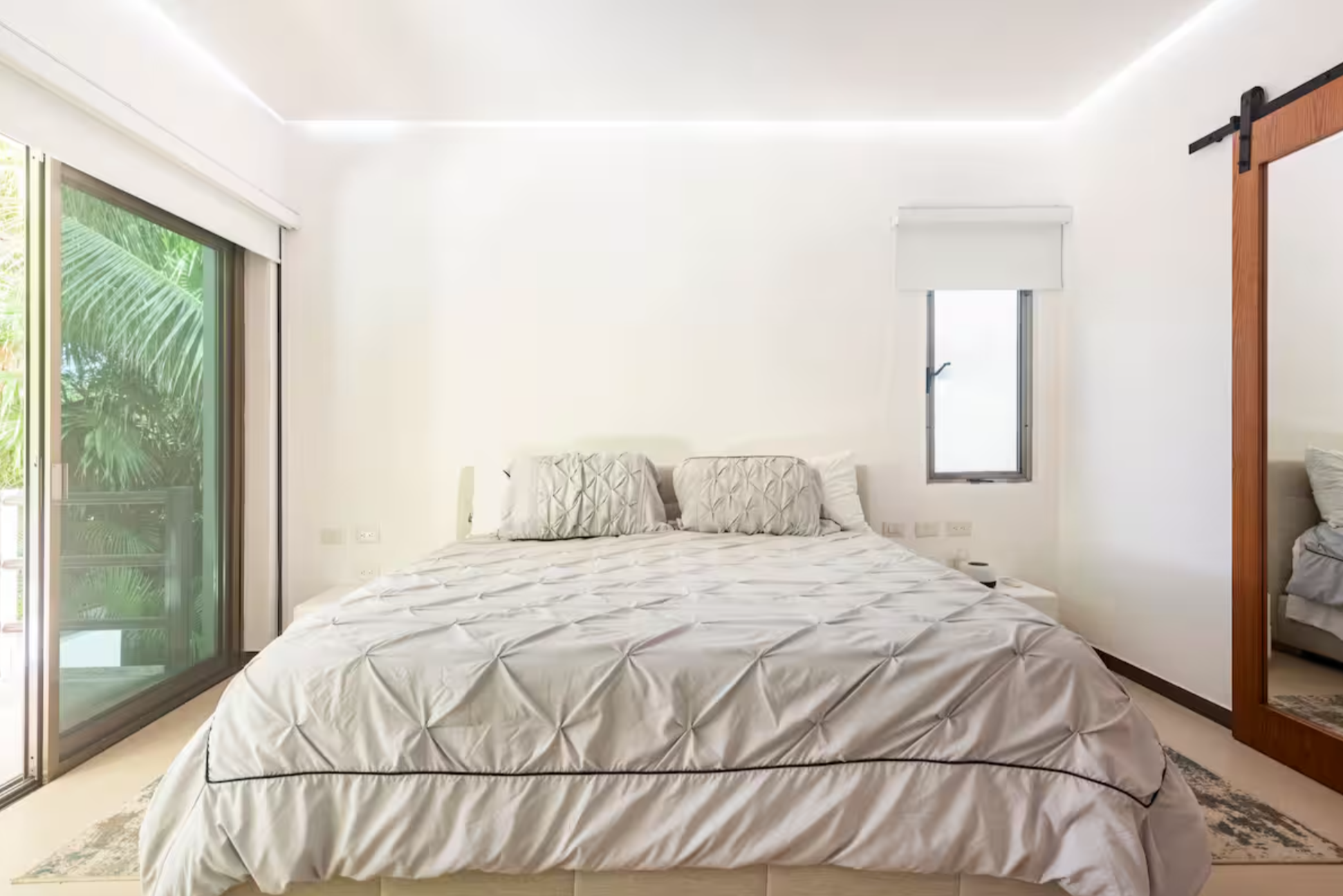 Minimalist bedroom with a large bed, white bedding, sliding glass door, and a wooden framed mirror.