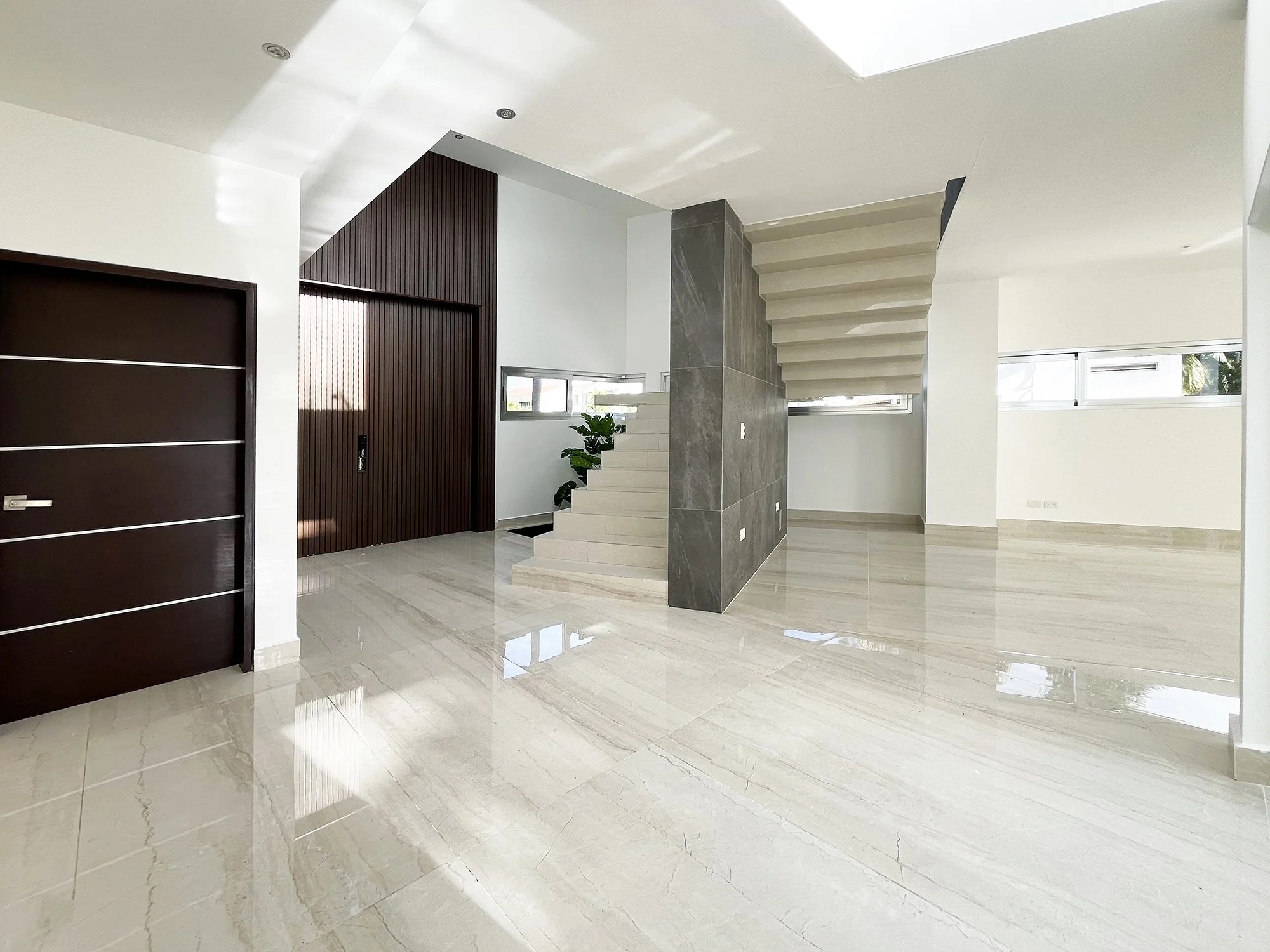 Modern minimalist interior with marble floors, a staircase, wooden door, and natural light through windows.