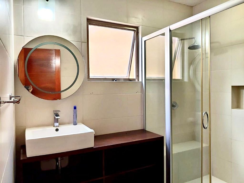 Modern bathroom with circular mirror, sink, and glass shower enclosure.