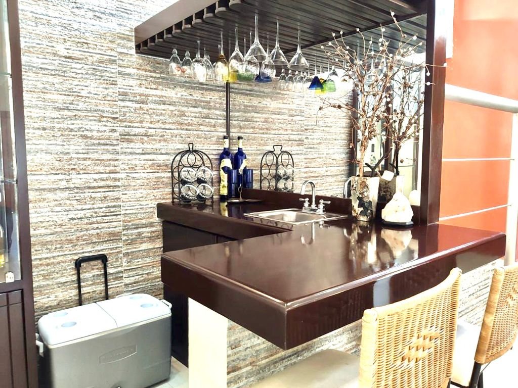 Home bar area with a counter, bar stools, and various decorative items, including hanging glasses, bottles, and a dry branch arrangement.
