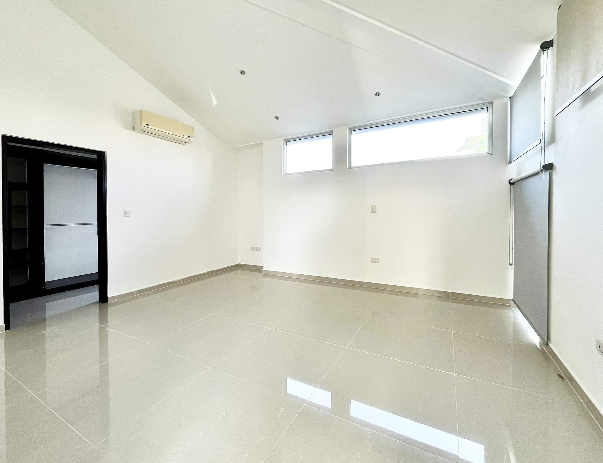 Bright empty room with tiled floor, high ceiling, air conditioner, rectangular windows, and a black-framed sliding door.